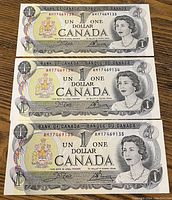 Front side view of three consecutive 1973 Canadian $1 bills showing Queen Elizabeth II portrait and serial numbers.