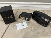 Three-piece lot showing vintage Pentax film camera, separate flash unit, and worn black storage box on floor.