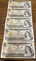 Front view of 5 Canadian one dollar bills from 1973 showing Queen Elizabeth II portrait and serial numbers.