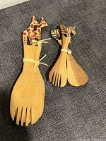 Two sets of wooden salad serving utensils tied together, one with giraffe head handles and one with zebra head handles, showing front view of forks and spoons.
