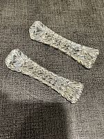 Two clear cut crystal chopstick holders placed on a textured dark fabric, showing the palmette and crosspiece pattern details.