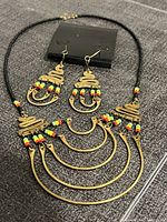 Close-up photo of Jamaican necklace and matching earrings showing the bead and metalwork details on a dark fabric background.