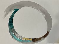 Close-up view of the abstract circular painting showing the brushstroke colors of gray, teal, gold, and brown on white paper.