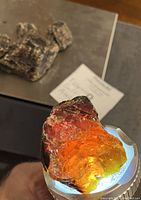 Close-up of a single raw amber stone held against a light source showing bright orange/red glow inside the amber.