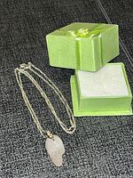 Photo showing rose quartz skull pendant necklace beside green velvet box with ribbon bow.