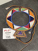 Full circular Maasai beaded necklace collar with colorful geometric beadwork and triangular pendant on grey fabric.