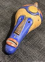 Front view of vintage handcrafted clay mask with vibrant blue, yellow, and orange colors. Texture visible on nose and facial features.