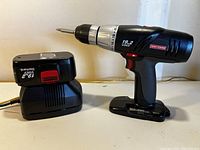 Wide side view of Craftsman 19.2 Volt cordless drill with attached rechargeable battery and charger next to it on tabletop.