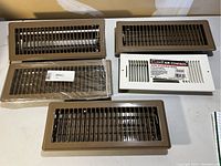 Top-down view of five heating vents; one white Leich Air Control register and four brown vents with horizontal slats.