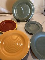 Group of assorted plates in earth tones, showing different colors and sizes arranged on a table.