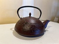 Side view of dark brown cast iron teapot showing embossed floral design and metal handle.