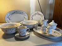 Set of Pfaltzgraff Winterberry dishes including bowls, cups, saucers, and serving pieces arranged on white table.