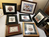 Seven framed prints including floral watercolor prints in dark green frames, two light wood framed prints of flower basket and polar bear with cardinals, plus one large dark wood framed floral and fruit print.