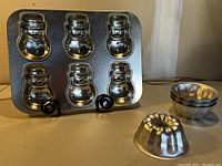 Photo showing one mini snowman cake tin with six snowman-shaped cake molds and four stacked mini Bundt pans with one Bundt pan front and center.