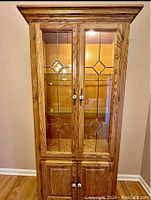 Front view of the solid oak curio cabinet showing glass doors with decorative diamond shaped leaded glass patterns and wood doors below.