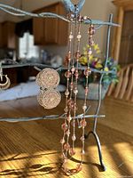 Two pairs of gold-toned earrings and a single-strand mixed metal bead necklace displayed on a metal jewelry tree. The necklace is shown doubled up.