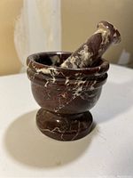 Front angle view of dark brown stone mortar and pestle showing marbling and stepped rim on mortar.