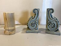Photo showing a standalone cream-colored stone bookend with brown marbled streaks alongside a moss green pair of carved floral and scrolling patterned bookends.