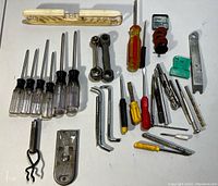All assorted tools arranged on a white surface, showing screwdrivers, wrenches, Allen keys, level, washers, and other hand tools.