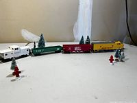 Full toy train set with the four train cars and assorted mini pine tree and fire hydrant decorations on a white surface
