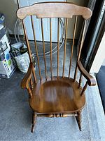 Front view of the vintage wooden rocking chair showing the contoured seat, spindle backrest, and armrests.
