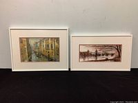 Two framed wall art pieces side by side, showing canal scenes in white frames with matting.