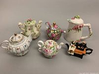 Five miniature porcelain and earthenware items displayed including four floral teapots/teacups and a sewing machine creamer