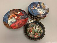 Photo of nine vintage decorative collectible plates featuring romantic and ballet scenes, and a Russian commemorative folk art plate with Cyrillic text.