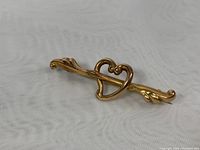 Angled front view of gold heart pin showing the open heart centered on a bar with delicate details.