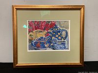 Framed watercolor painting featuring a still life of blue and yellow teapot, sugar bowl, and creamer with red flowers in the background.