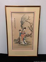 Full view of the framed Chinese watercolour painting showing two women in traditional attire near a blossoming tree, with silk mat border and bamboo-style frame.