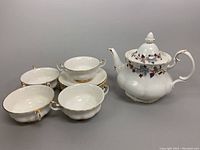 Photo of 4 Val Dor bone china double-handle cream soup bowls with matching saucers arranged next to a Lorraine teapot with floral design and gold trim.