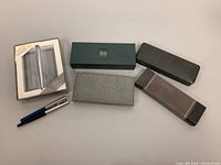 Lot overview with all pens, pencils, and cases displayed on flat surface.