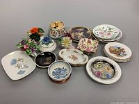 Various vintage assorted hand painted porcelain chinaware including plates, dishes, and decorative floral porcelain pieces, displayed on gray background.