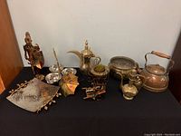 Overview of all items on black cloth against a white background including knight figure, serving pieces, kettle, ewer, bowls, and other metal decorative items.
