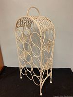 Front and side views of vintage wrought iron wine rack showing decorative scrollwork, floral medallion details on sides, lattice barrel-shaped top and distressed paint finish.