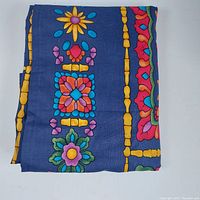 Folded handcrafted multicolor tablecloth showing part of the floral and geometric pattern on a navy blue background.