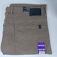 Folded taupe colored men's denim jeans with visible back pocket and size tag showing 40x30 size.