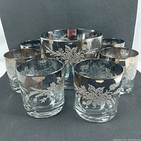 Photo showing 1 glass ice bucket and 6 lowball glasses arranged in a group, all featuring silver floral decoration.