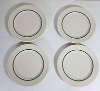 Four white Syracuse China plates arranged in a square showing front face with green decorative ring near inner edge.