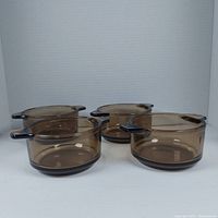 Four amber-colored round glass casserole dishes with handles, shown from side angle.