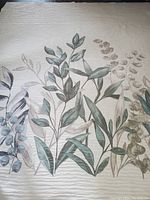 Close-up of one side of the bedspread showing cream background with multi-colored botanical leaf print.