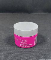 Bright pink jar of StriVectin Multi-Action Restorative Cream with silver lid, showing branding and product text against a black textured background.