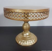 Front view of the metal commercial cake stand showing decorative lattice side and the pedestal base, gold colored, unused.