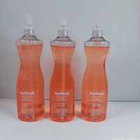 Three bottles of orange liquid dish soap with pump dispensers, front view and label visible.