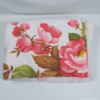 Folded large beach towel showing vivid pink and red flower print with green leaves on white background.