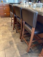 Three brown faux leather bar stools placed at kitchen counter showing their backs and legs.