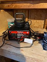 Photo showing MotoMaster battery charger with Power Probe III automotive circuit tester on a wood shelf.