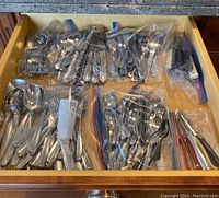 Top-down view of kitchen drawer with multiple plastic bags containing assorted cutlery and utensils.