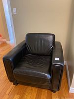 Front view of one dark brown leather club chair showing creases and wear on seat and back cushions.